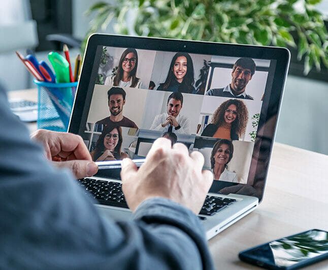 Male employee speaking on video call with diverse colleagues on online briefing with laptop at home.